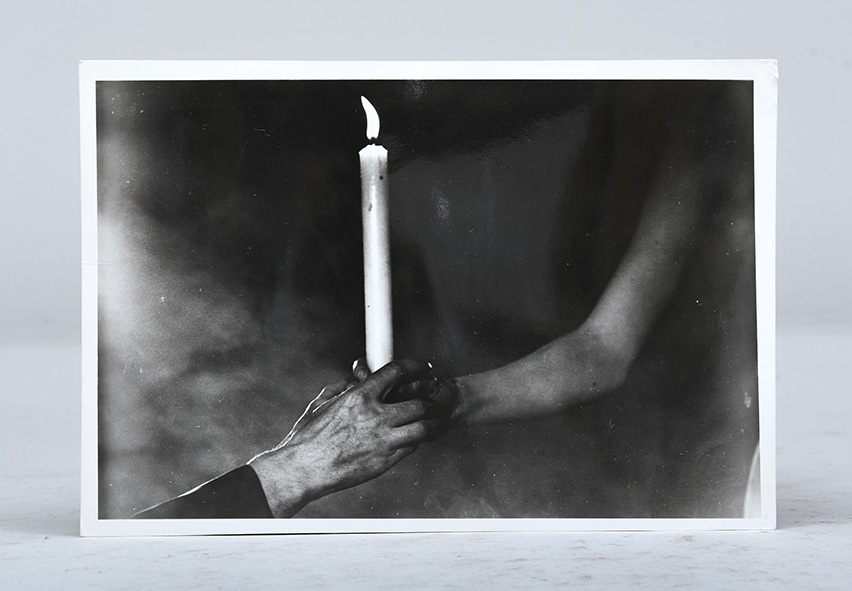 Two hands reaching out and grasping a lit candle.